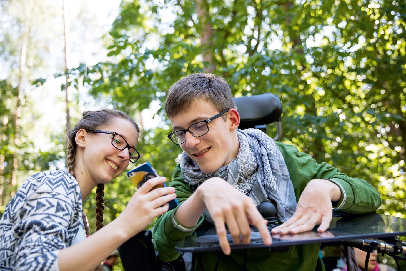 Eine Jugendliche zeigt einem jungen Mann im Rollstuhl etwas auf ihrem Handy.